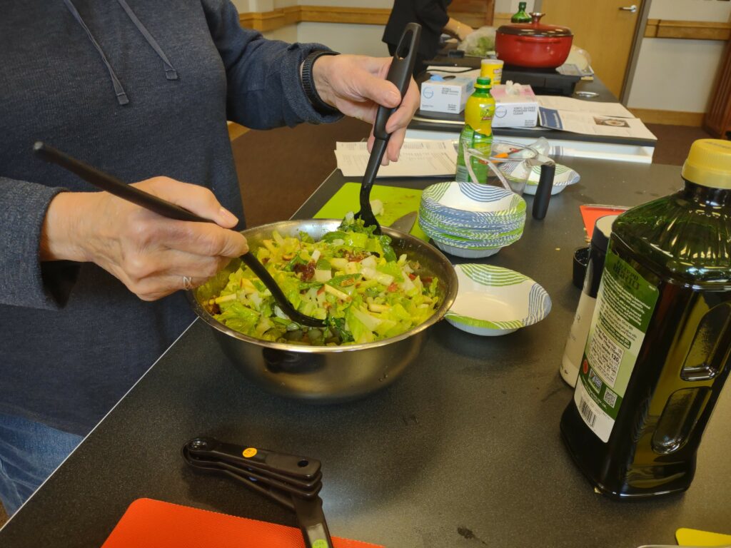 A green salad is tossed in a metal bowl with a vinaigrette. 